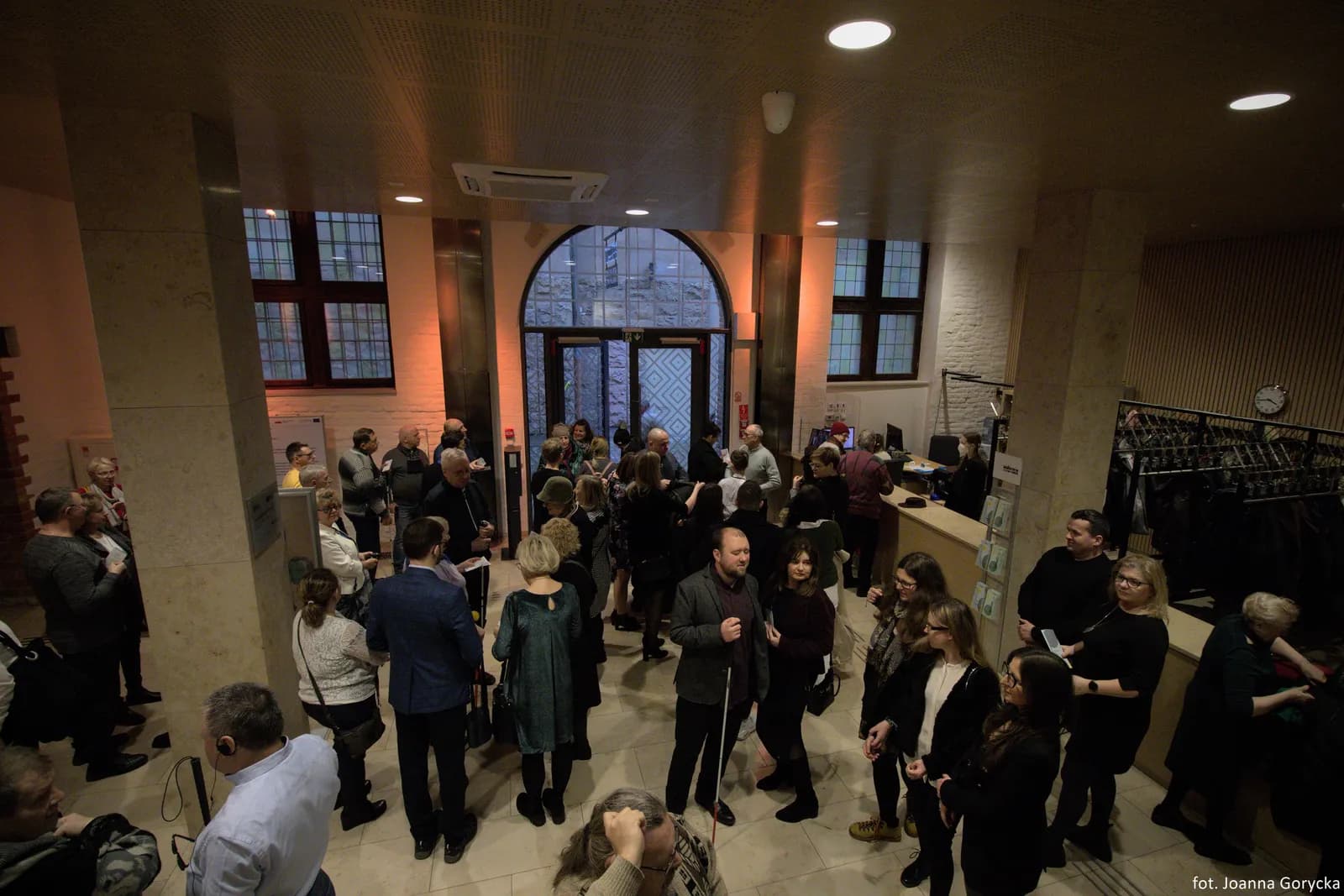 Widzowie w oczekiwaniu na spektakl na foyer Starej Apteki. Widok z góry. Wśród tłumu osoby z białymi laskami i w ciemnych okularach.